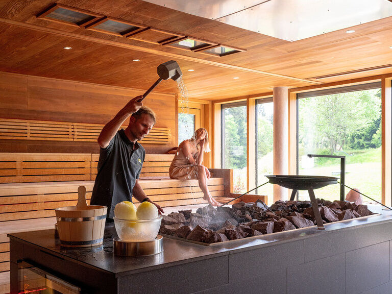 Ein Saunameister steht vor der Aufgussstation der finnischen Stubensauna des Wellnesshotels Mooshof im Bayerischen Wald und heizt die Sauna ein.