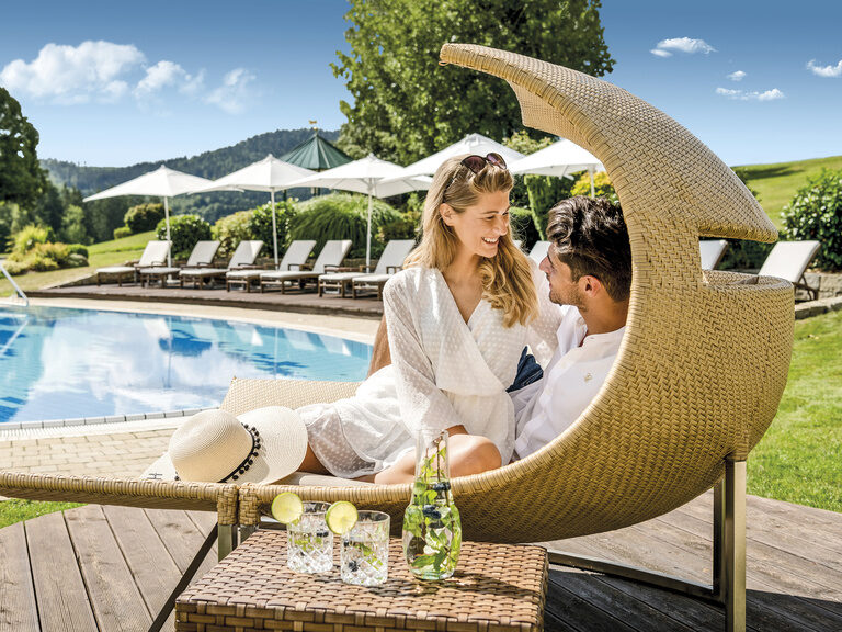 Ein lächelndes Paar genießt einen sonnigen Tag am Außepool des Wellness & SPA Resort Mooshof