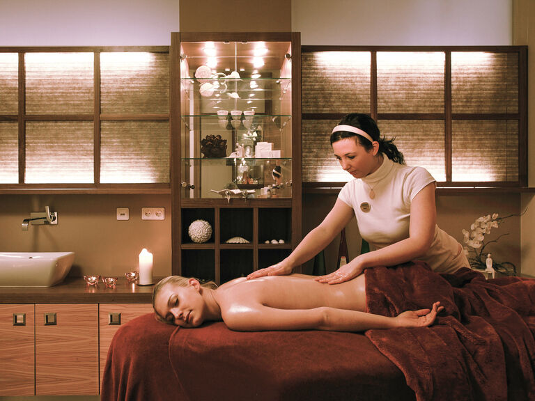 Eine entspannte Frau auf einem Behandlungsbett in dem Wellnessraum des Hotels Mooshof in Bayern.