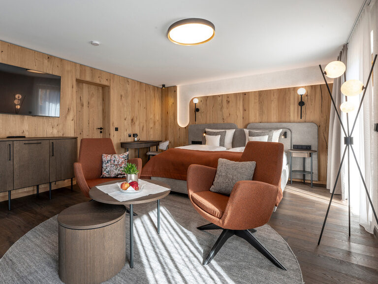 Großräumiger Wohnbereich mit strahlender Beleuchtung und Flachbildfernseher - Zimmer Typ 3 im Hotel Mooshof in Bayern.